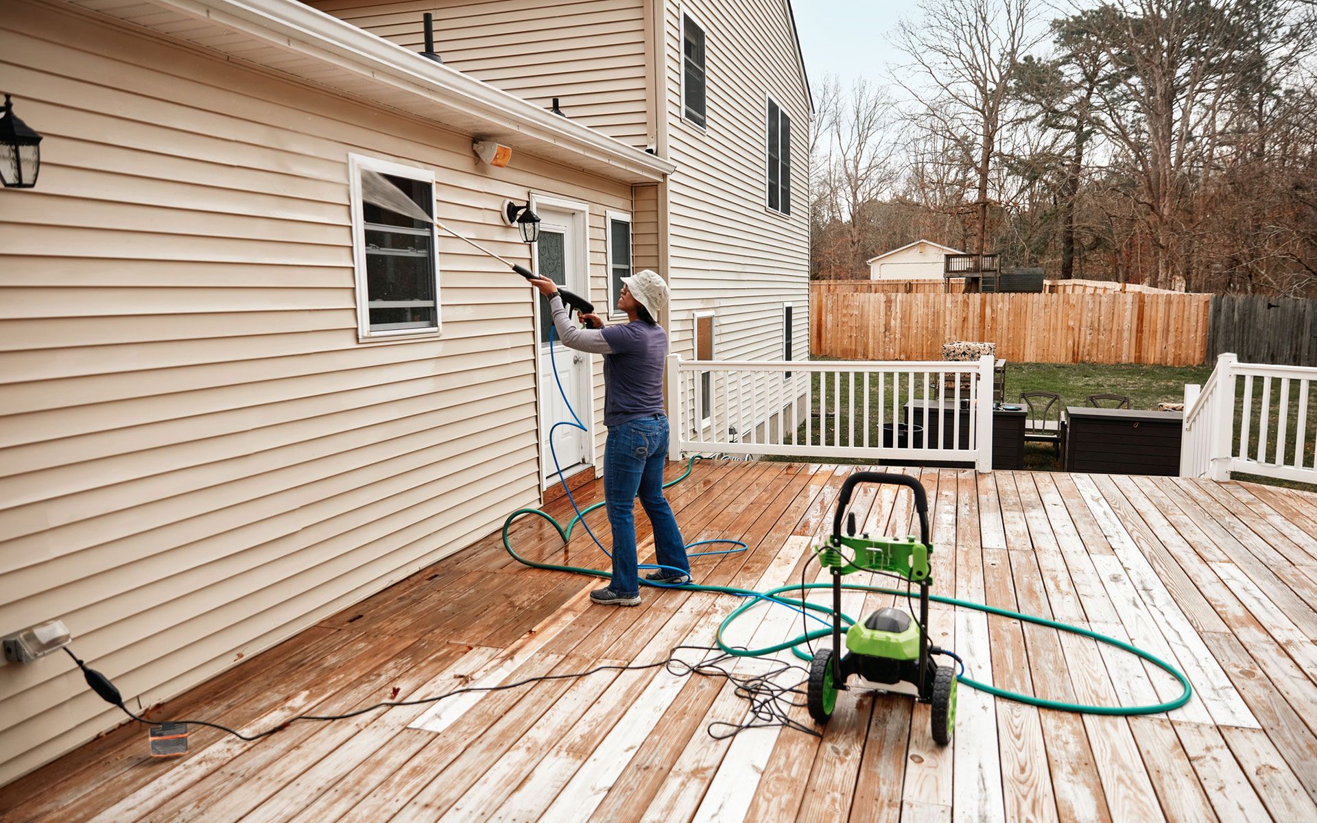 A man is cleaning the side of a house with a pressure washer.