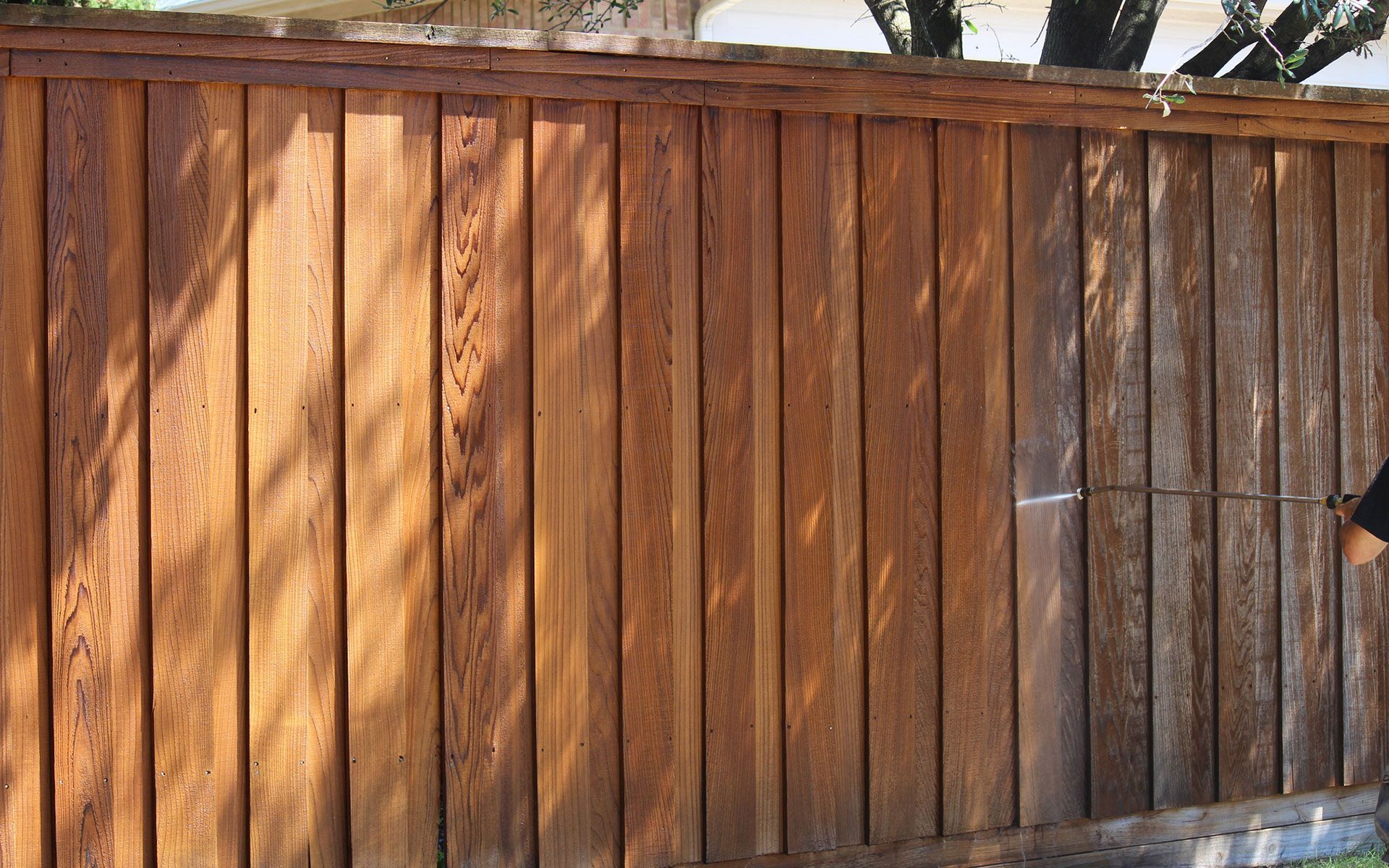 A person is cleaning a wooden fence with a high pressure washer.