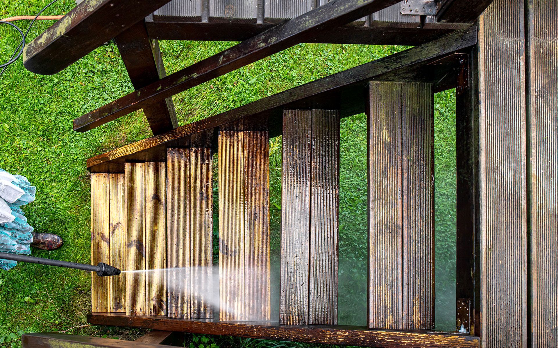 A person is cleaning a wooden deck with a high pressure washer.