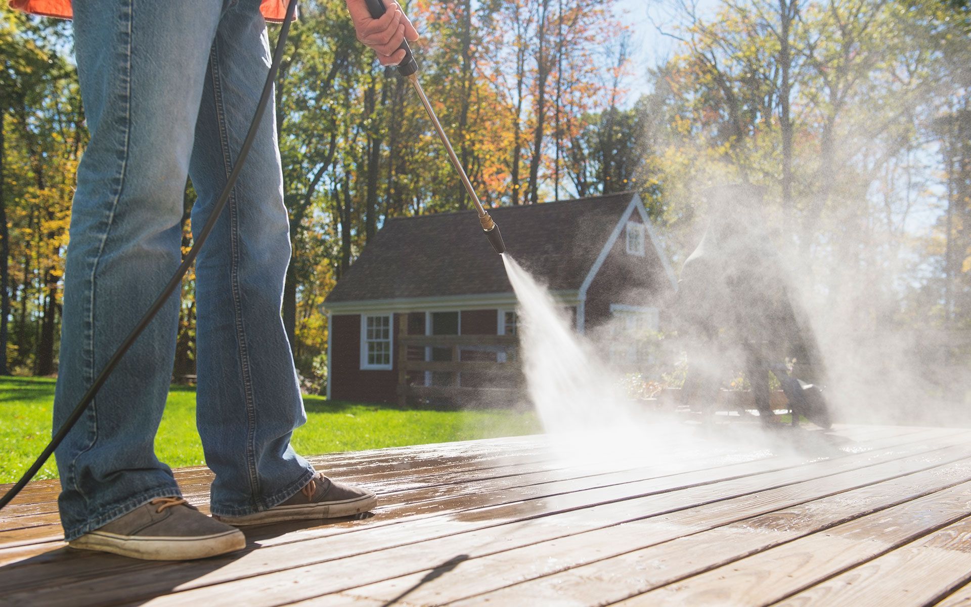 A man is using a high pressure washer to clean a wooden deck.