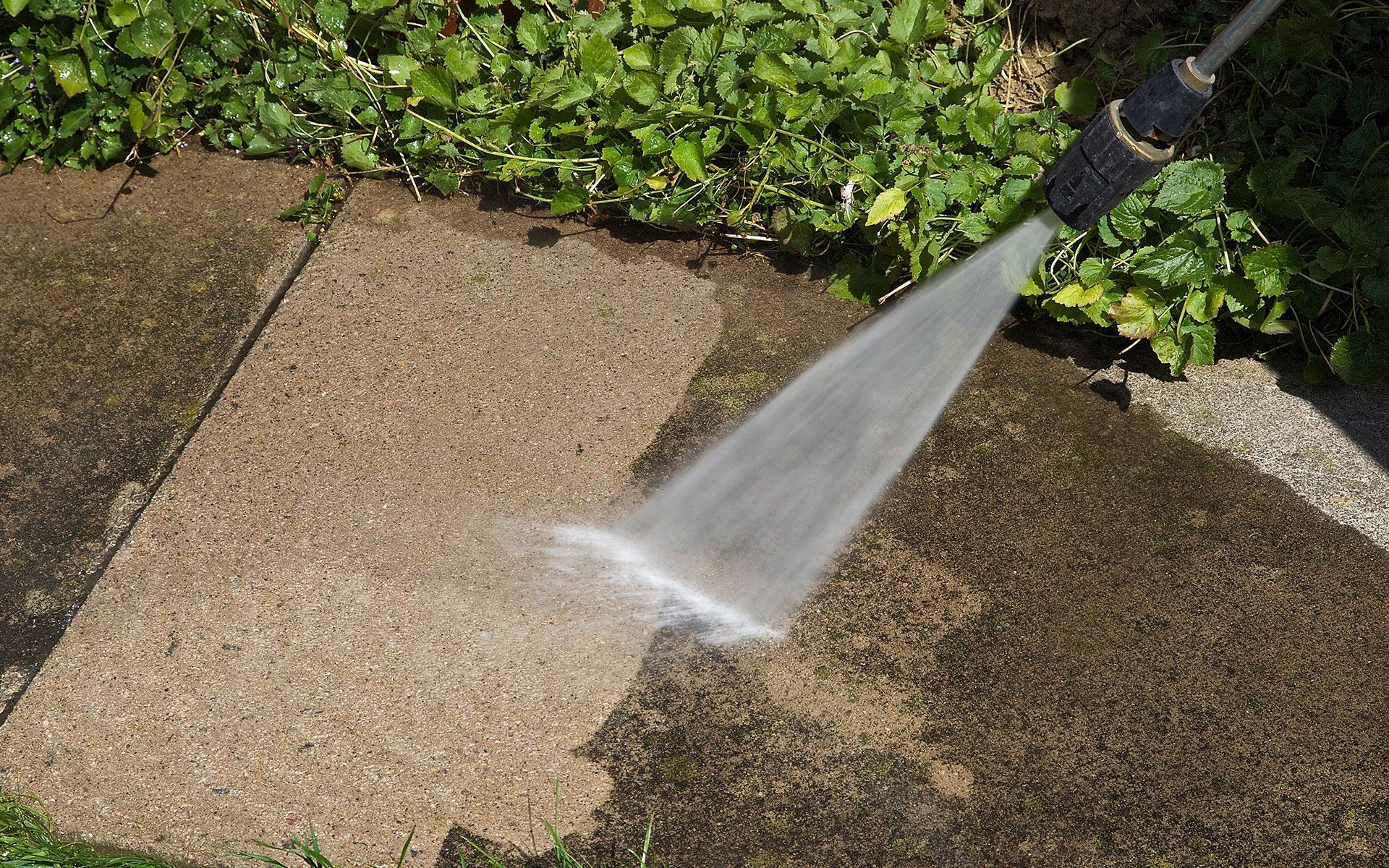 A person is using a high pressure washer to clean a sidewalk.