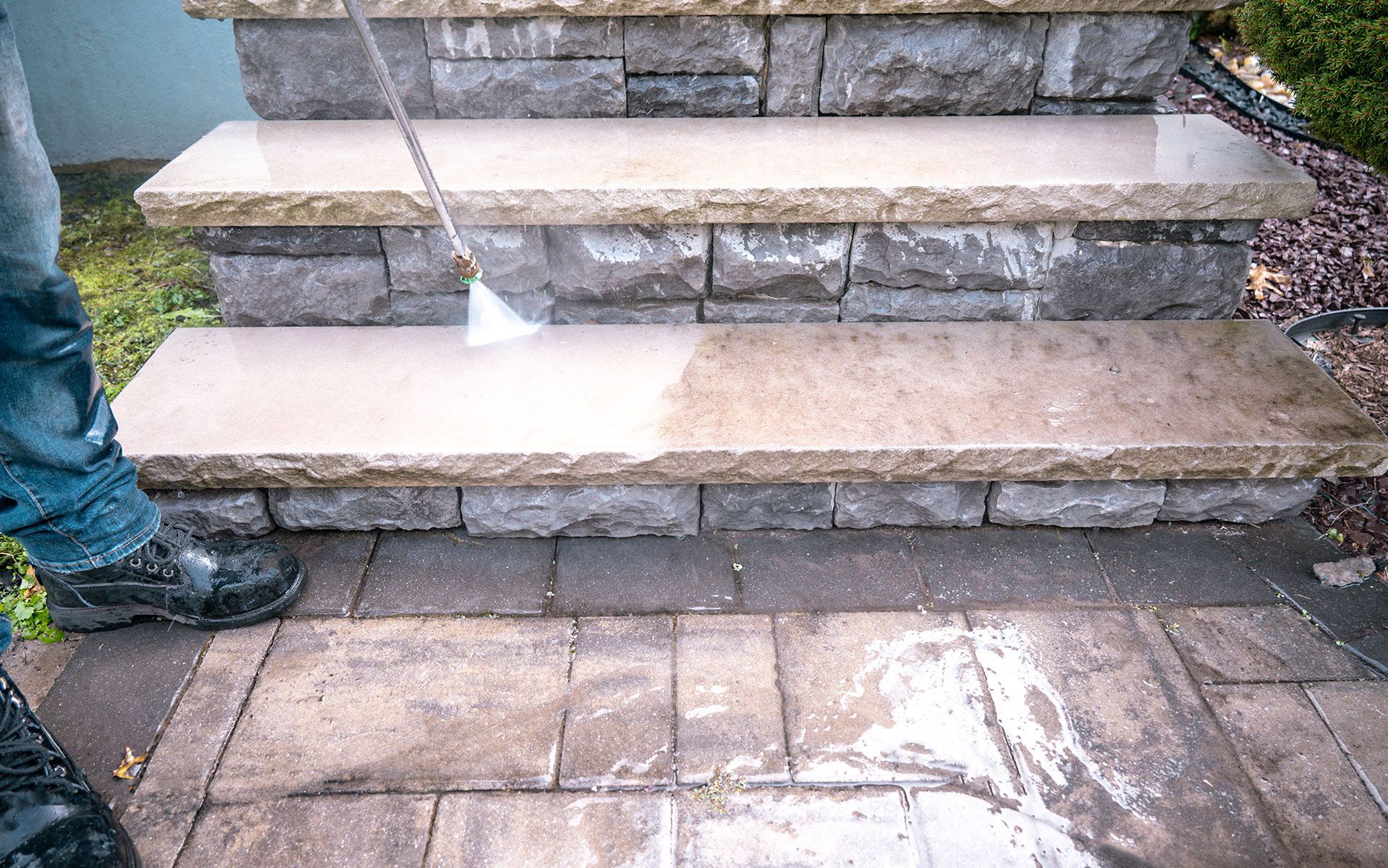 A person is cleaning a stone staircase with a high pressure washer.