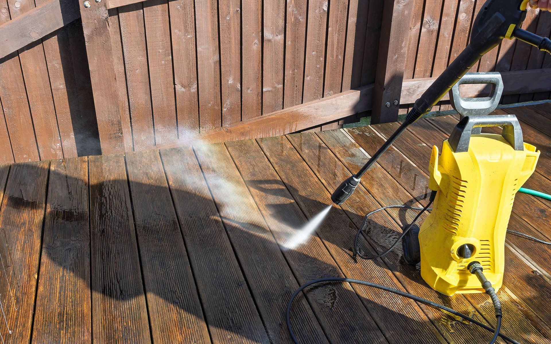A person is using a high pressure washer to clean a wooden deck.