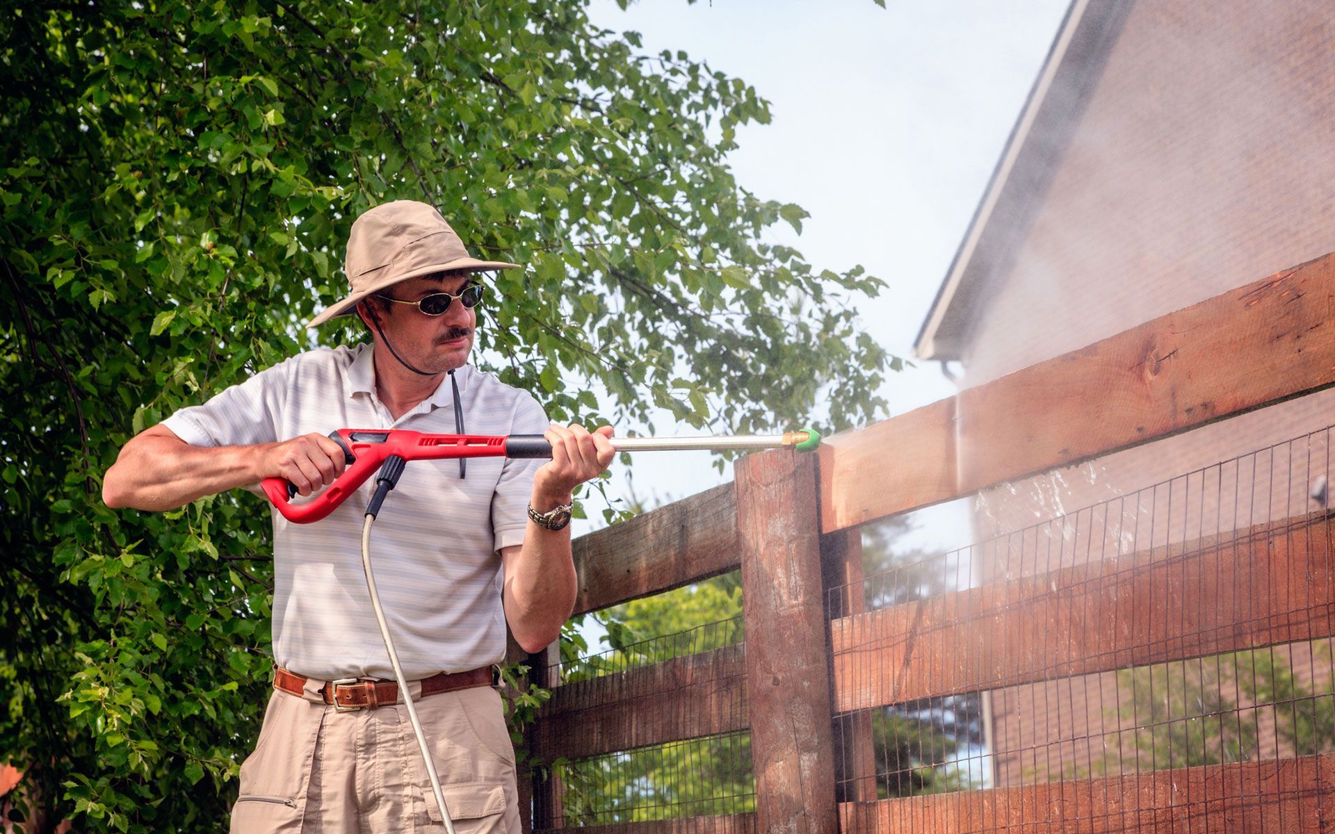 A man is cleaning a wooden fence with a high pressure washer.