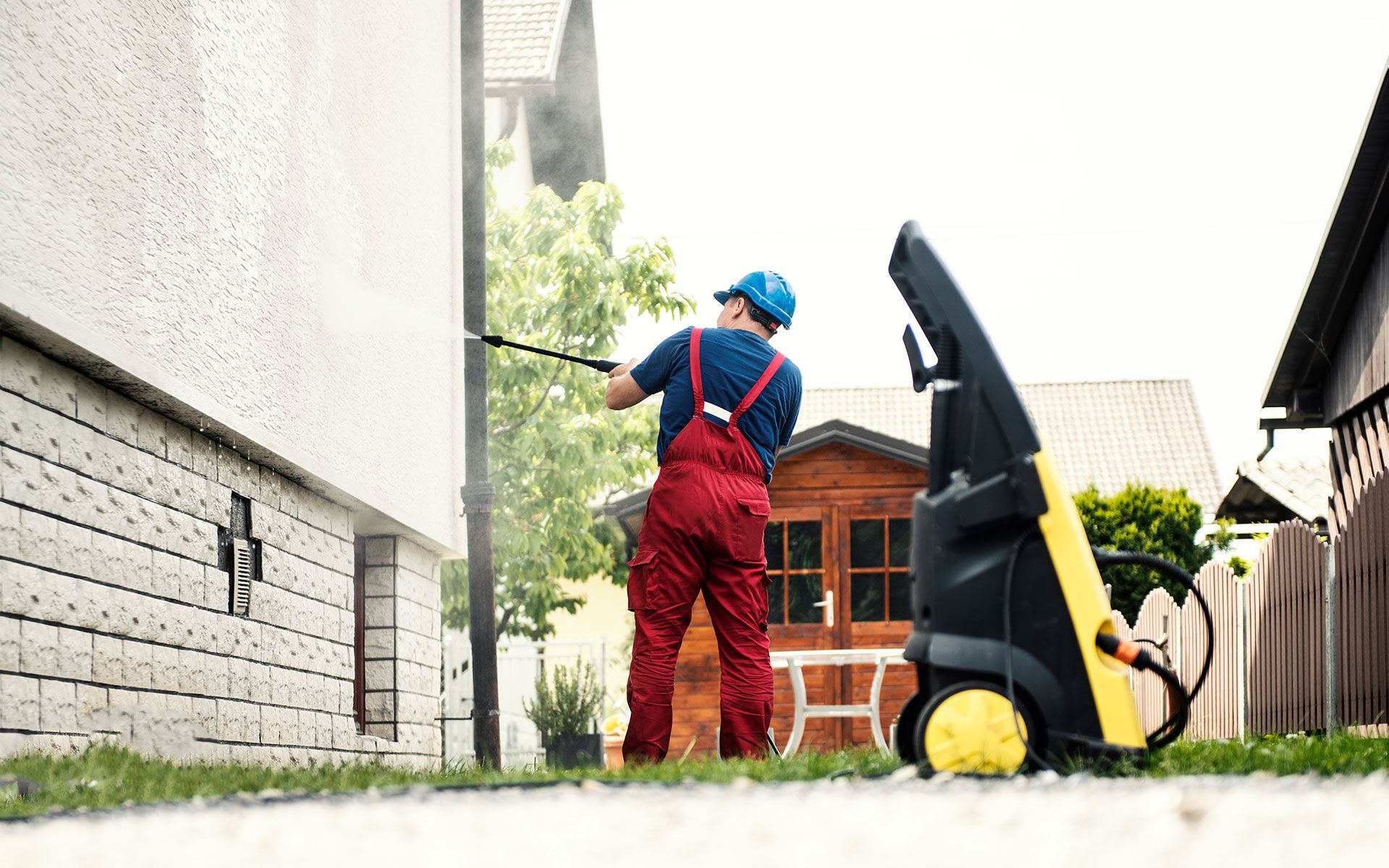 A man is using a high pressure washer to clean the side of a building.