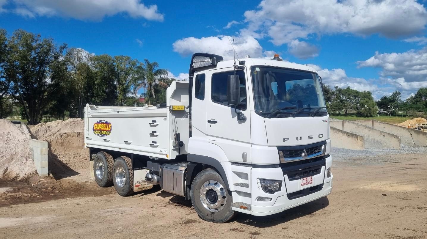 A white dump truck is parked in a dirt lot.