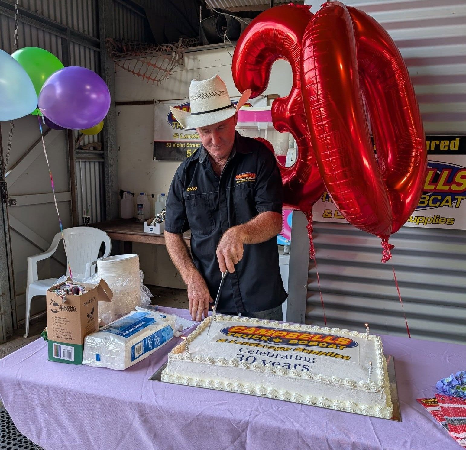 A man is cutting a cake with balloons in the background