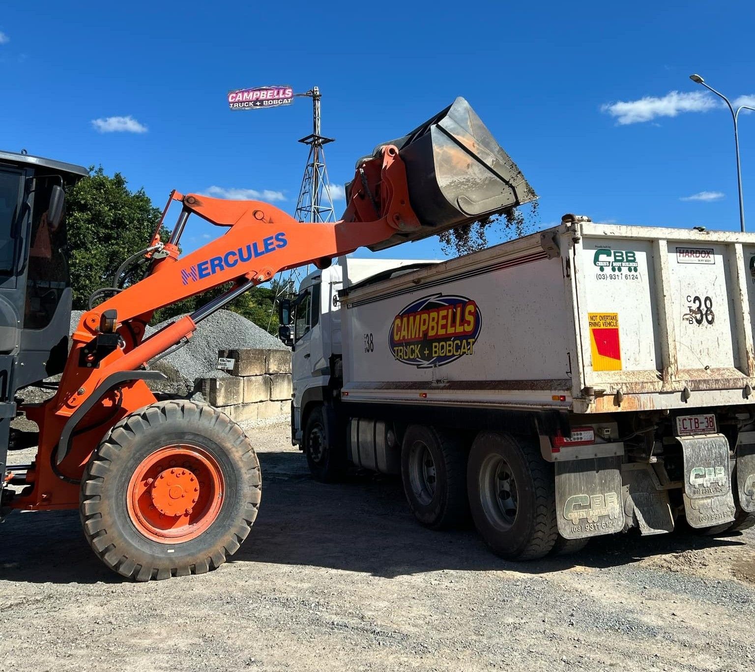 A hercules loader is loading dirt into a dump truck