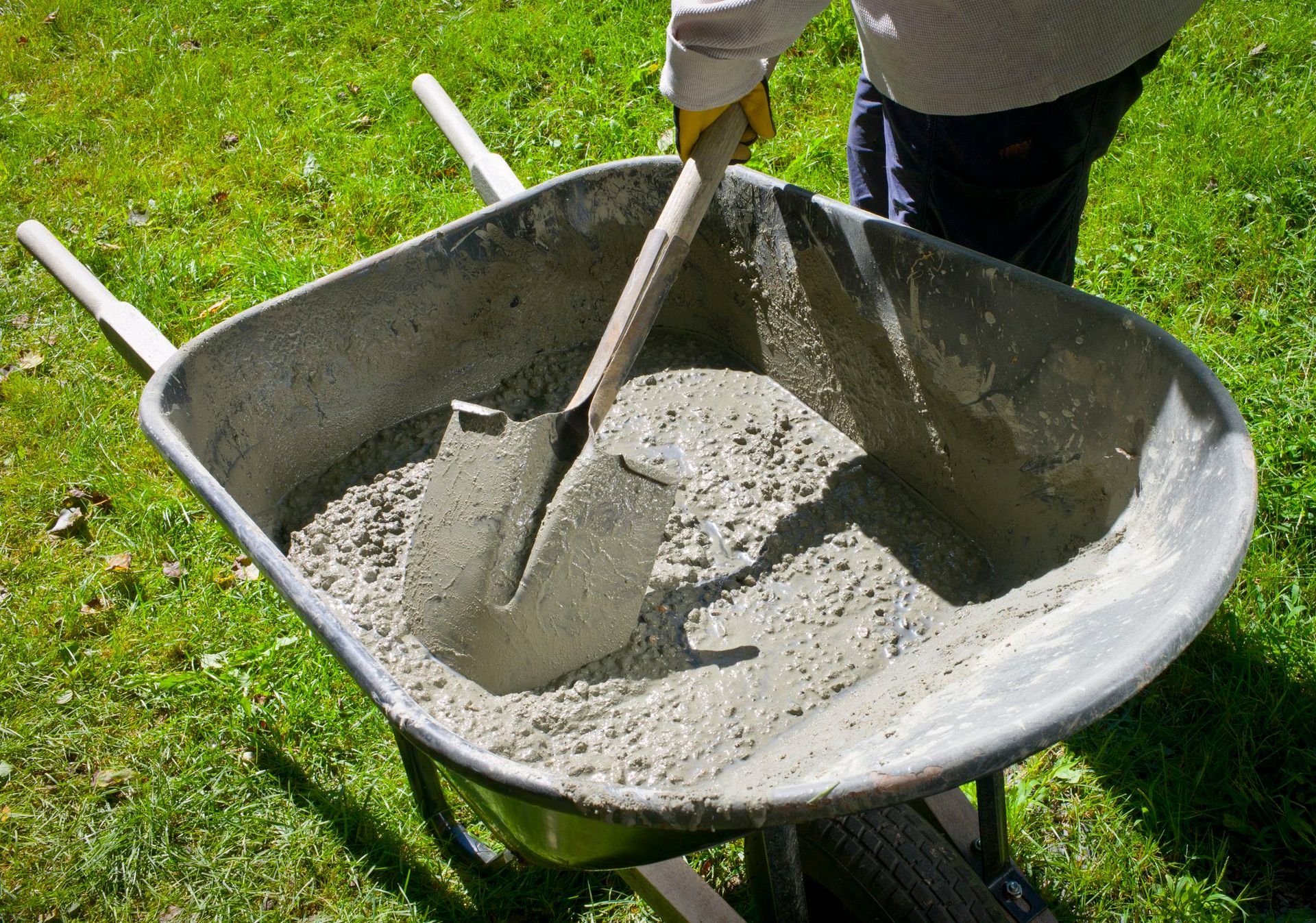 A person is mixing concrete in a wheelbarrow with a shovel.