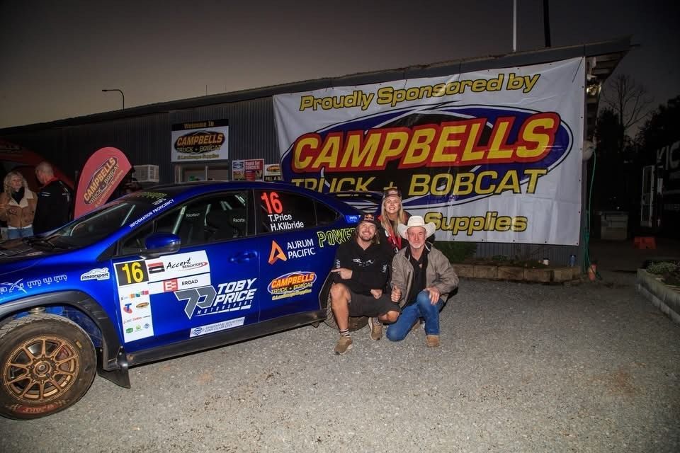 Blue rally car with three people posing in front of a banner for Campbell's Truck & Bobcat Supplies.
