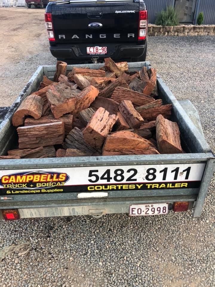 A Trailer Filled With Logs is Parked Next to a Truck — Campbell's Truck and Bobcat and Landscape Supplies In Gympie, QLD