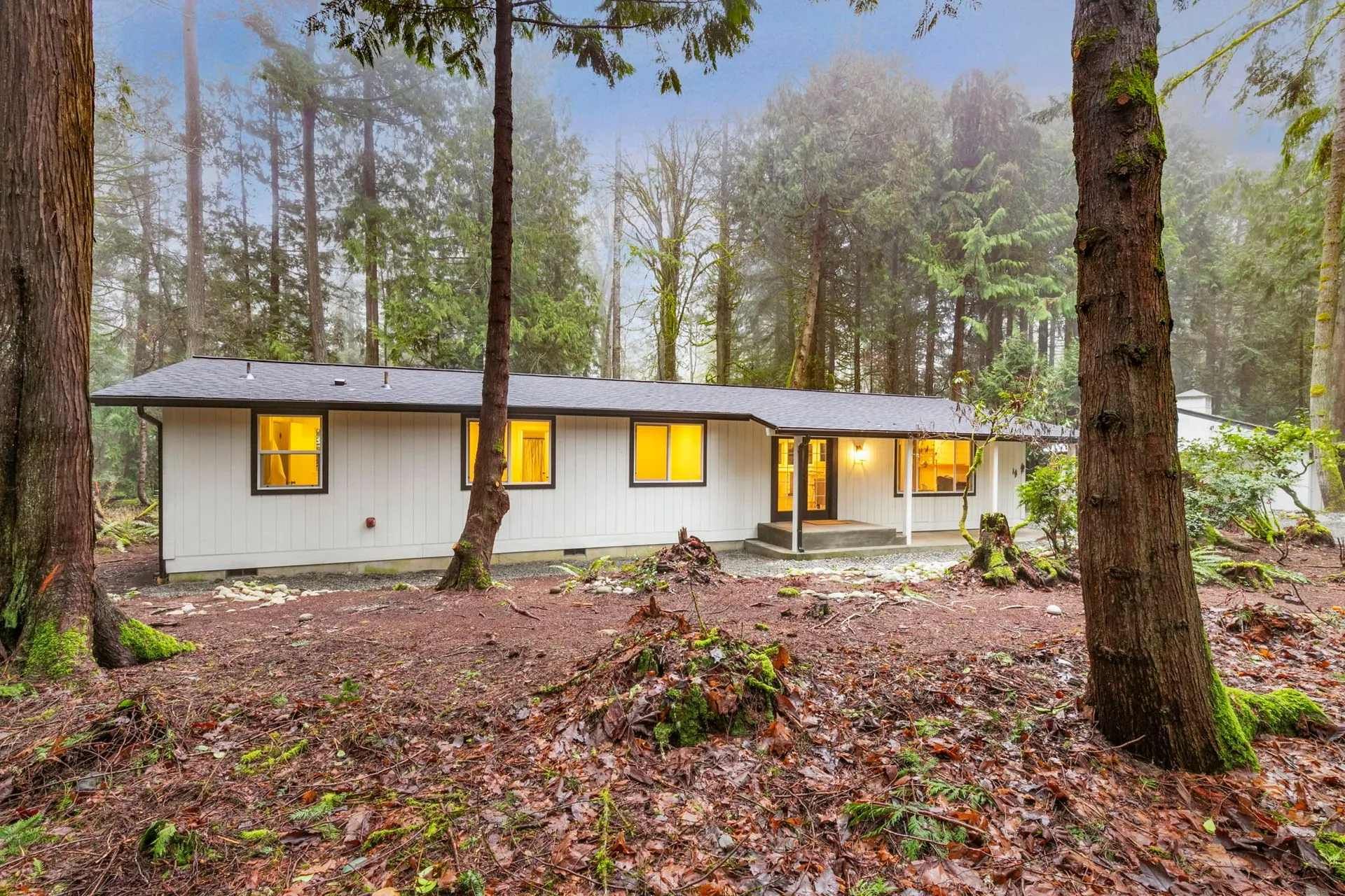 A white house is surrounded by trees in the middle of a forest.