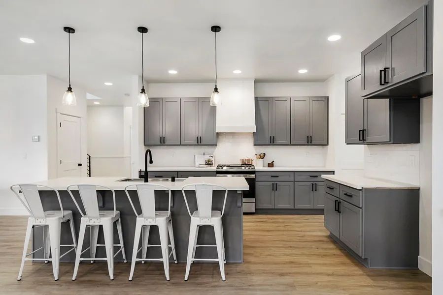 A kitchen with gray cabinets and white counter tops and stools.