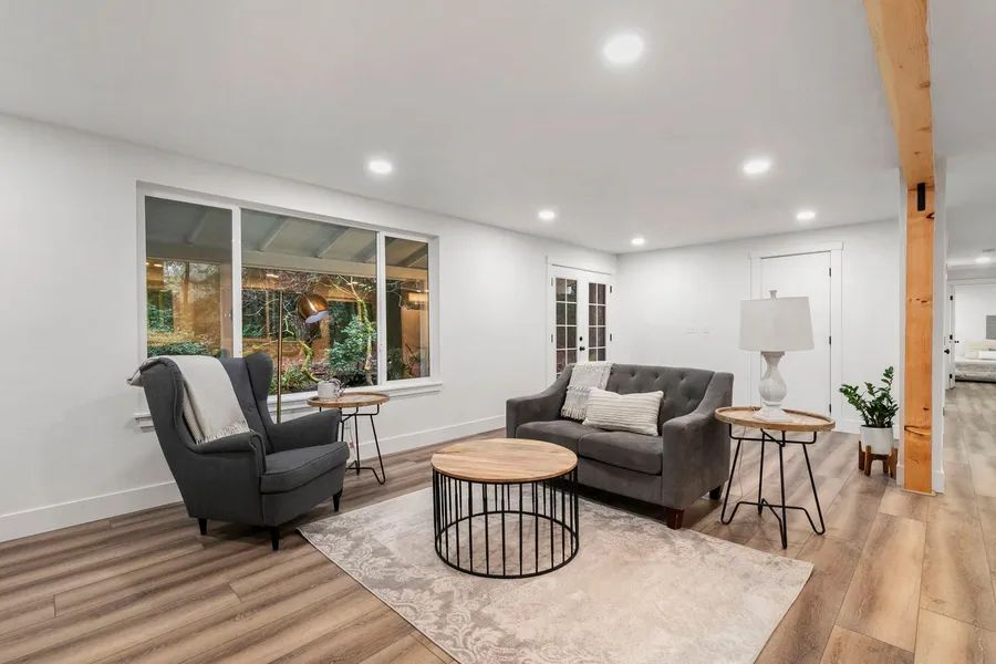 A living room with a couch , chairs , tables and a large window.