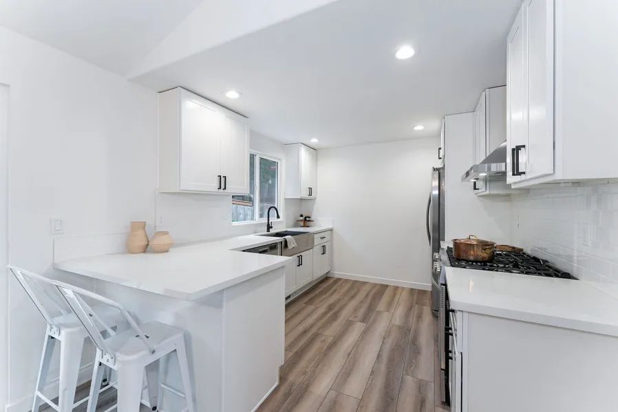 A kitchen with white cabinets , stainless steel appliances , hardwood floors and a stove.