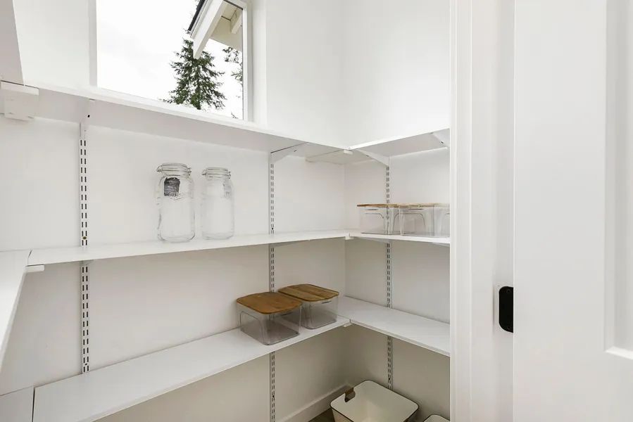 A pantry with white shelves and a window in a house.