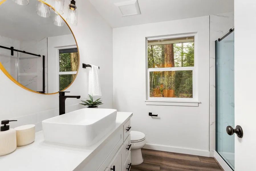 A bathroom with a sink , toilet , mirror and window.