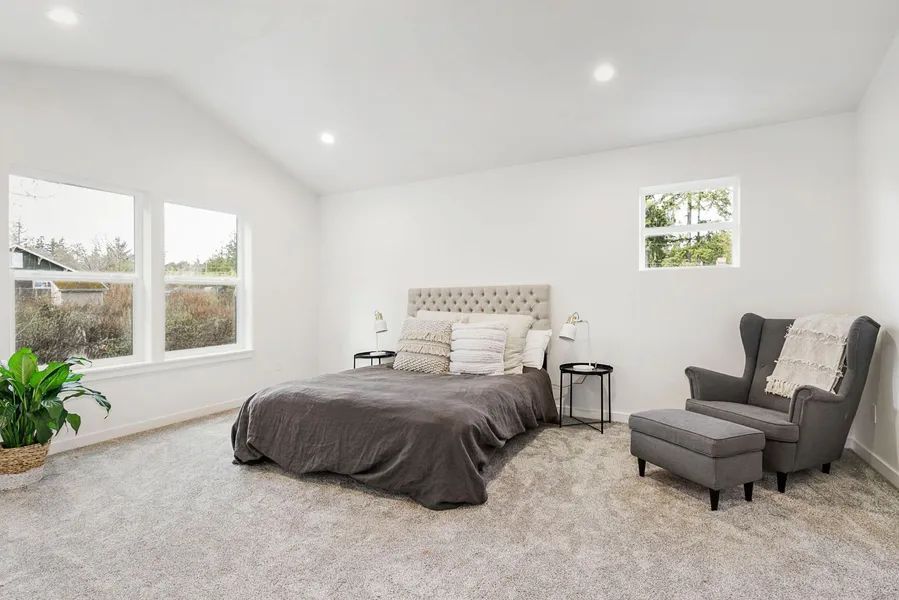 A bedroom with a bed , chair , ottoman and window.