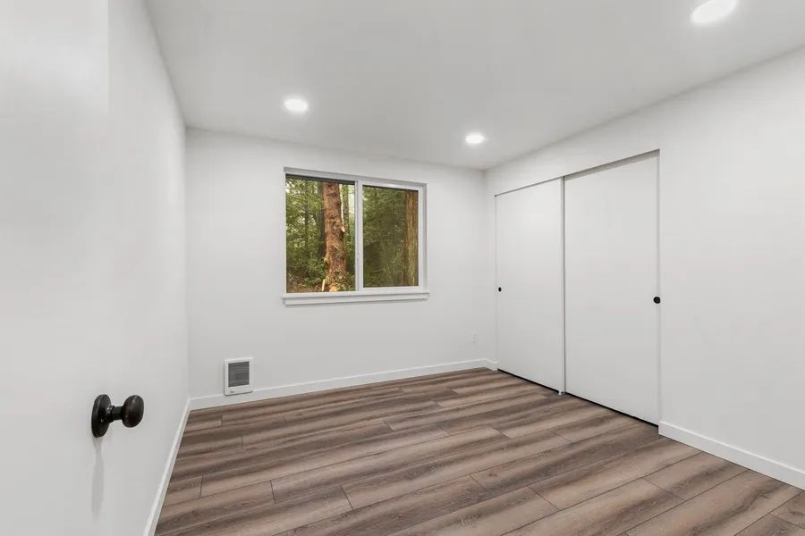 An empty room with hardwood floors , white walls and a window.