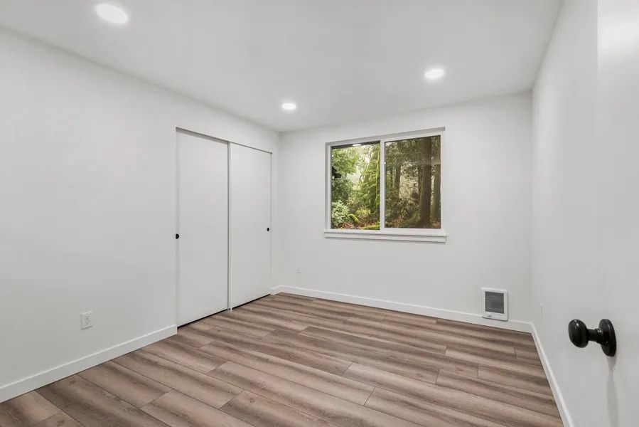 An empty room with hardwood floors , white walls and a window.