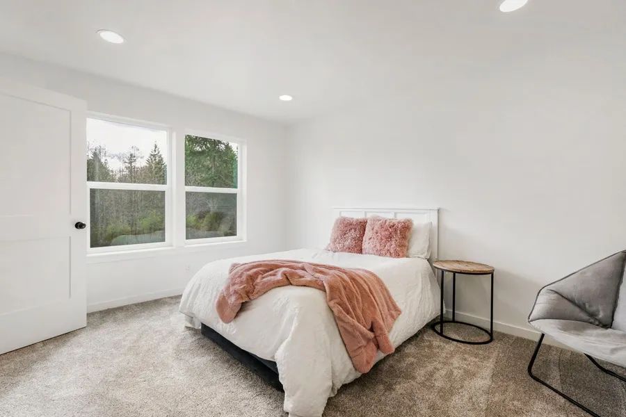 A bedroom with a bed , chair , table and two windows.