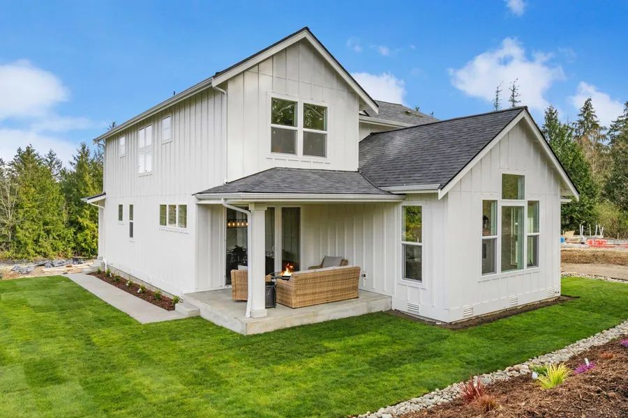 A white house with a black roof is sitting on top of a lush green field.