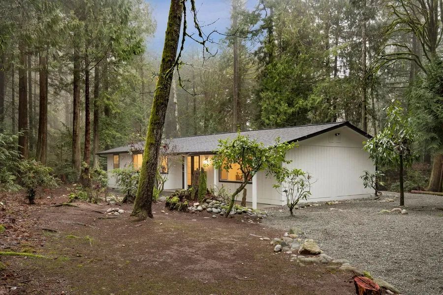 A white house is surrounded by trees in the middle of a forest.