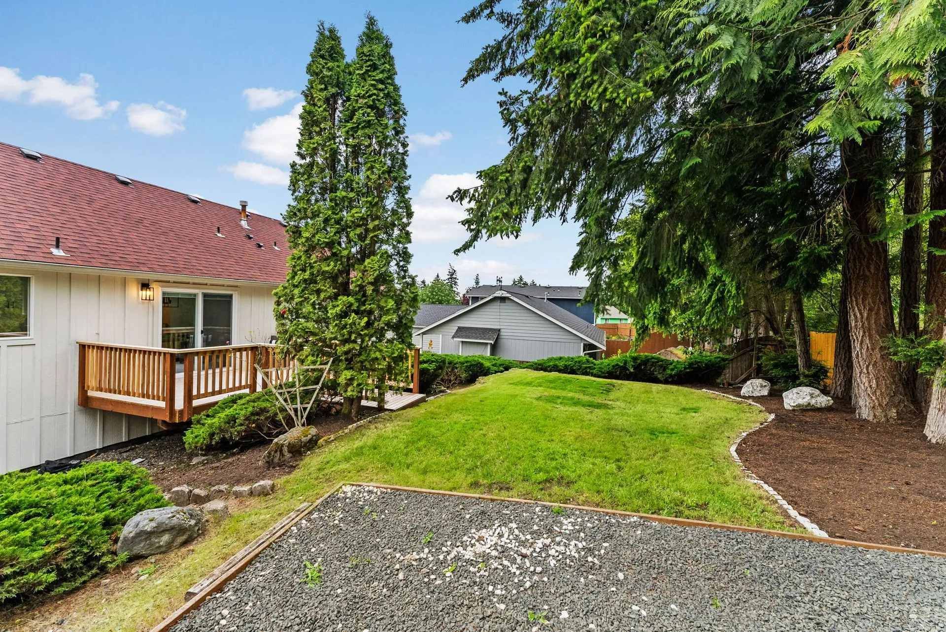 A white house with a red roof is surrounded by trees and a gravel driveway.