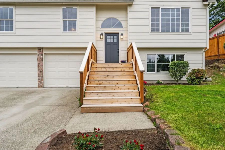 A white house with a wooden deck and stairs leading up to the front door.