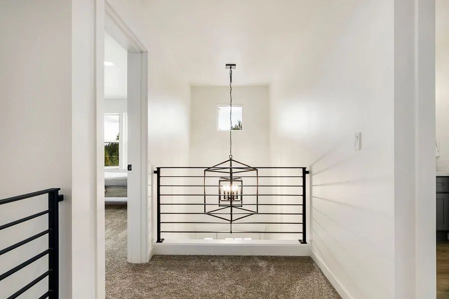 A hallway with a black railing and a chandelier hanging from the ceiling.