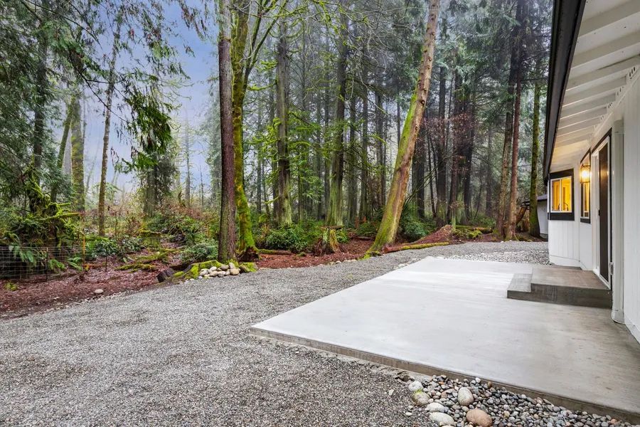 A white house with a gravel driveway leading to it in the middle of a forest.