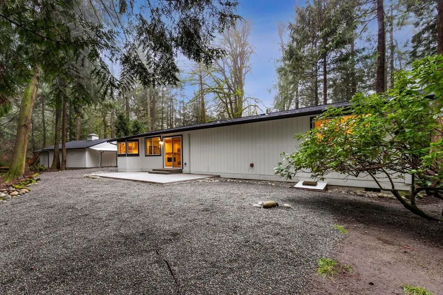 A white house is surrounded by trees and gravel in the middle of a forest.