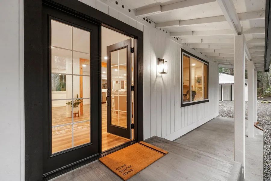 A white house with black sliding glass doors and a welcome mat on the porch.