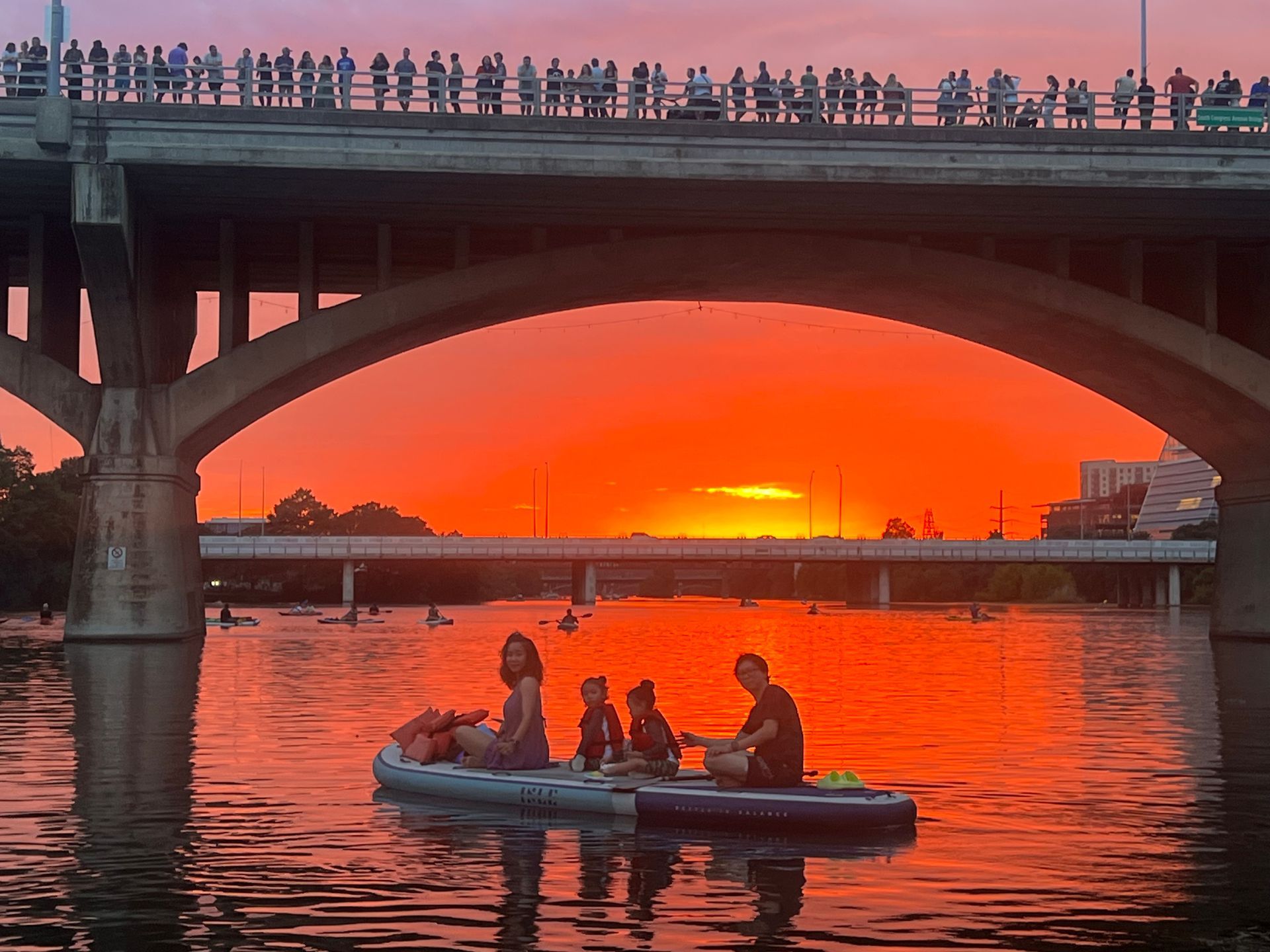 Small paddleboarding group at sunset on Lady Bird Lake with calm water reflections