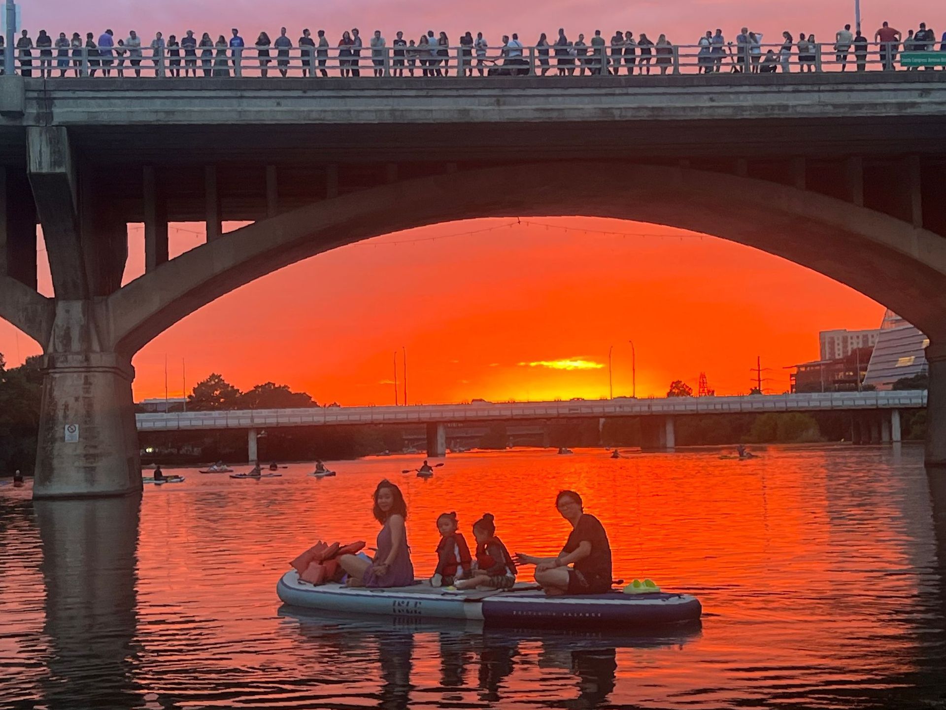 A group of people in a kayak under the Congress bridge at sunset