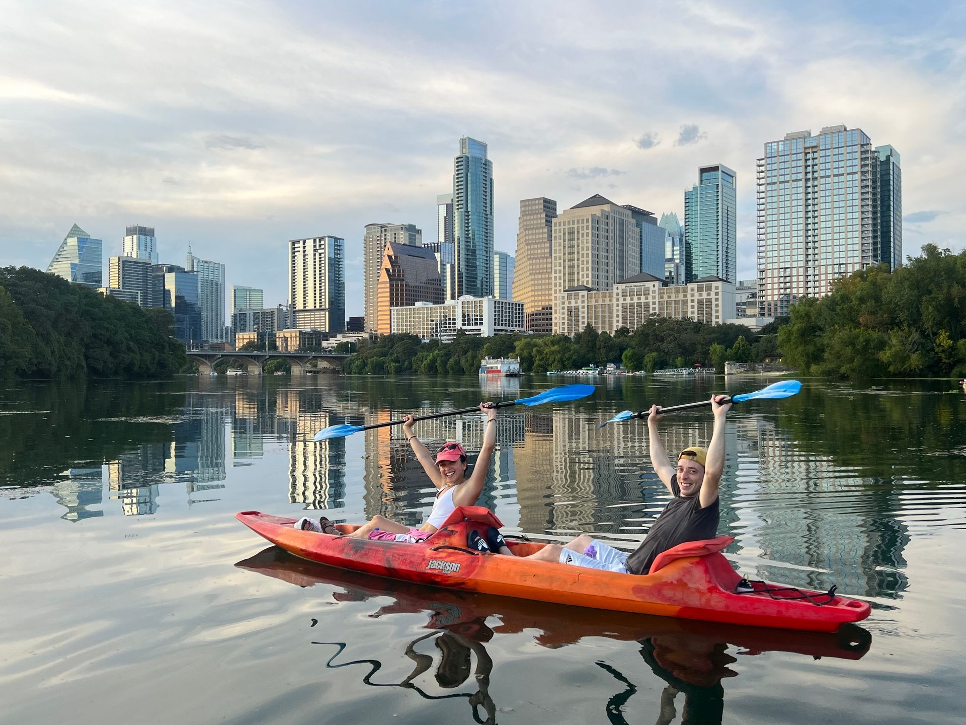 A man is paddling a kayak on a river in front of tall buildings.
