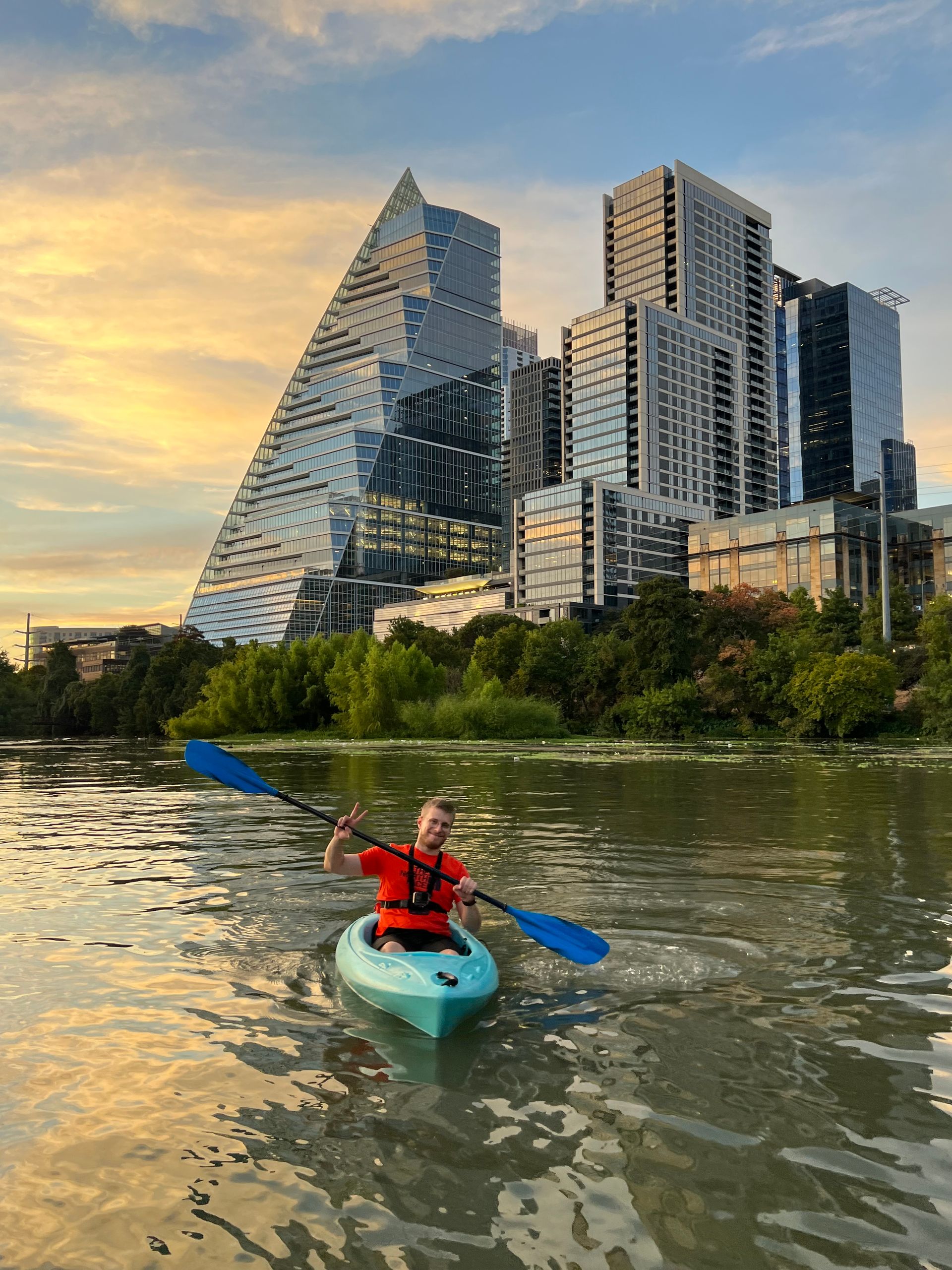 A man is paddling a kayak on a river in front of tall buildings.