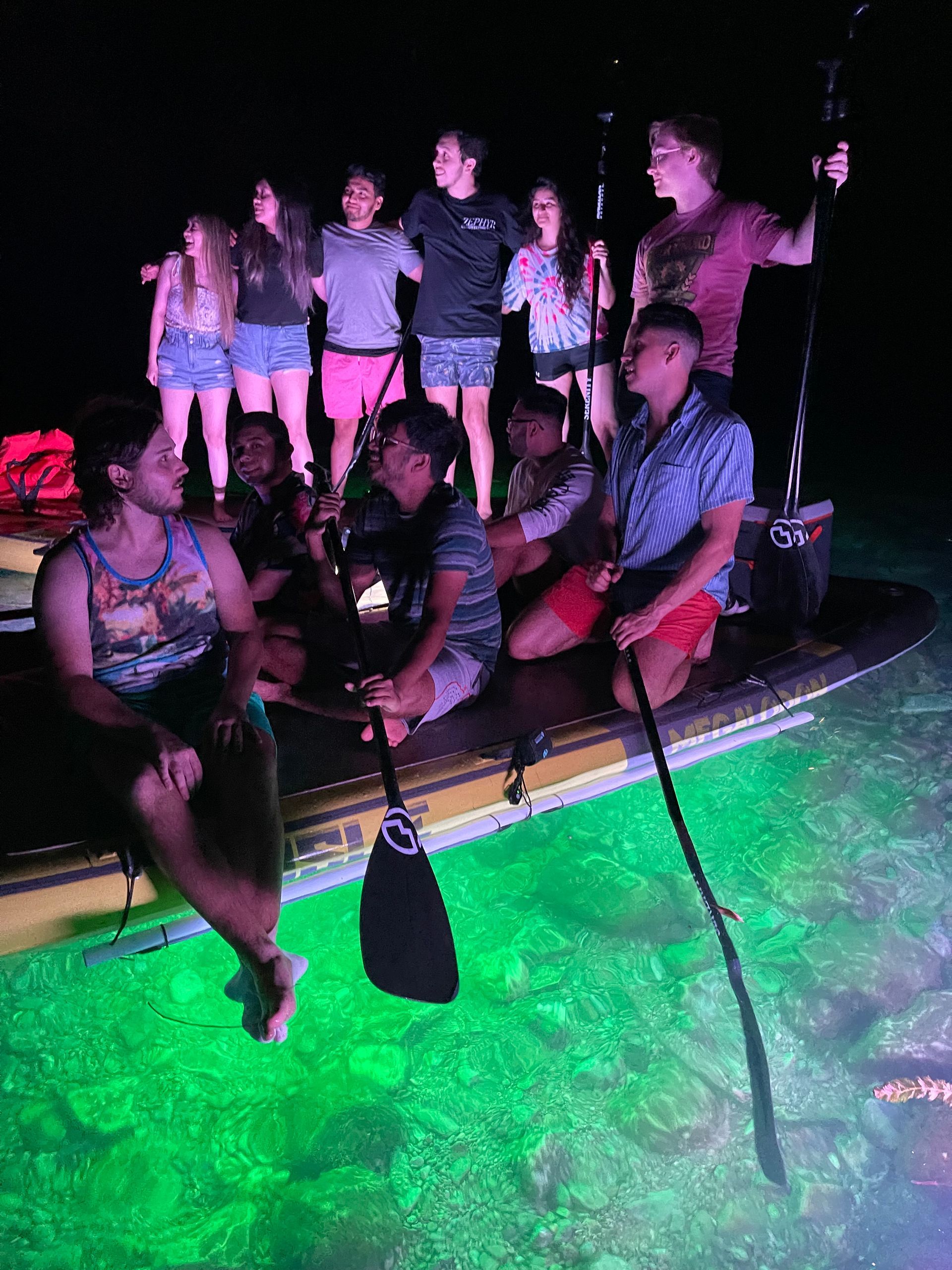 A group of people are sitting on a paddleboard in the water at night.