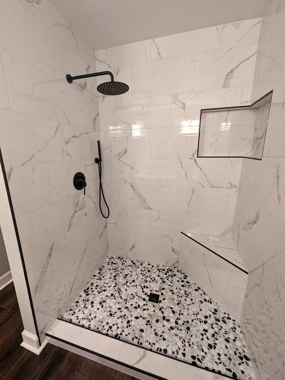 A walk in shower with a shower head and a tiled floor.