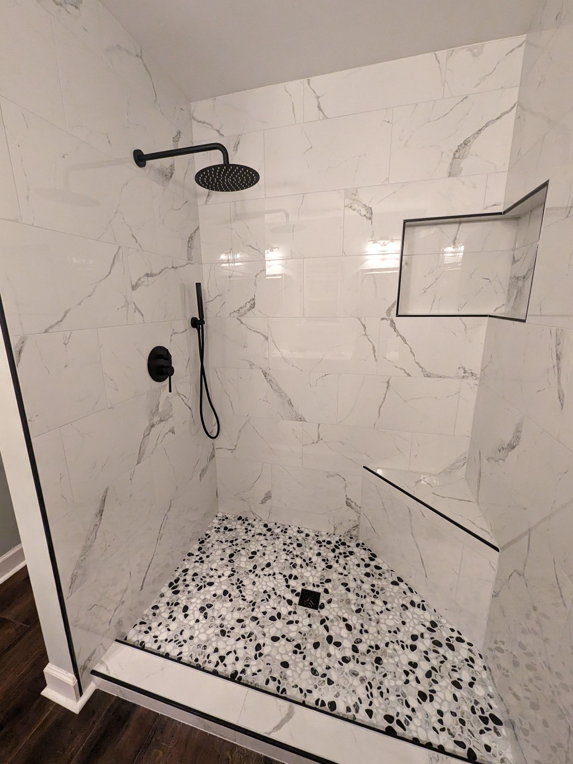 A walk in shower with a shower head and a tiled floor that was a full shower remodel