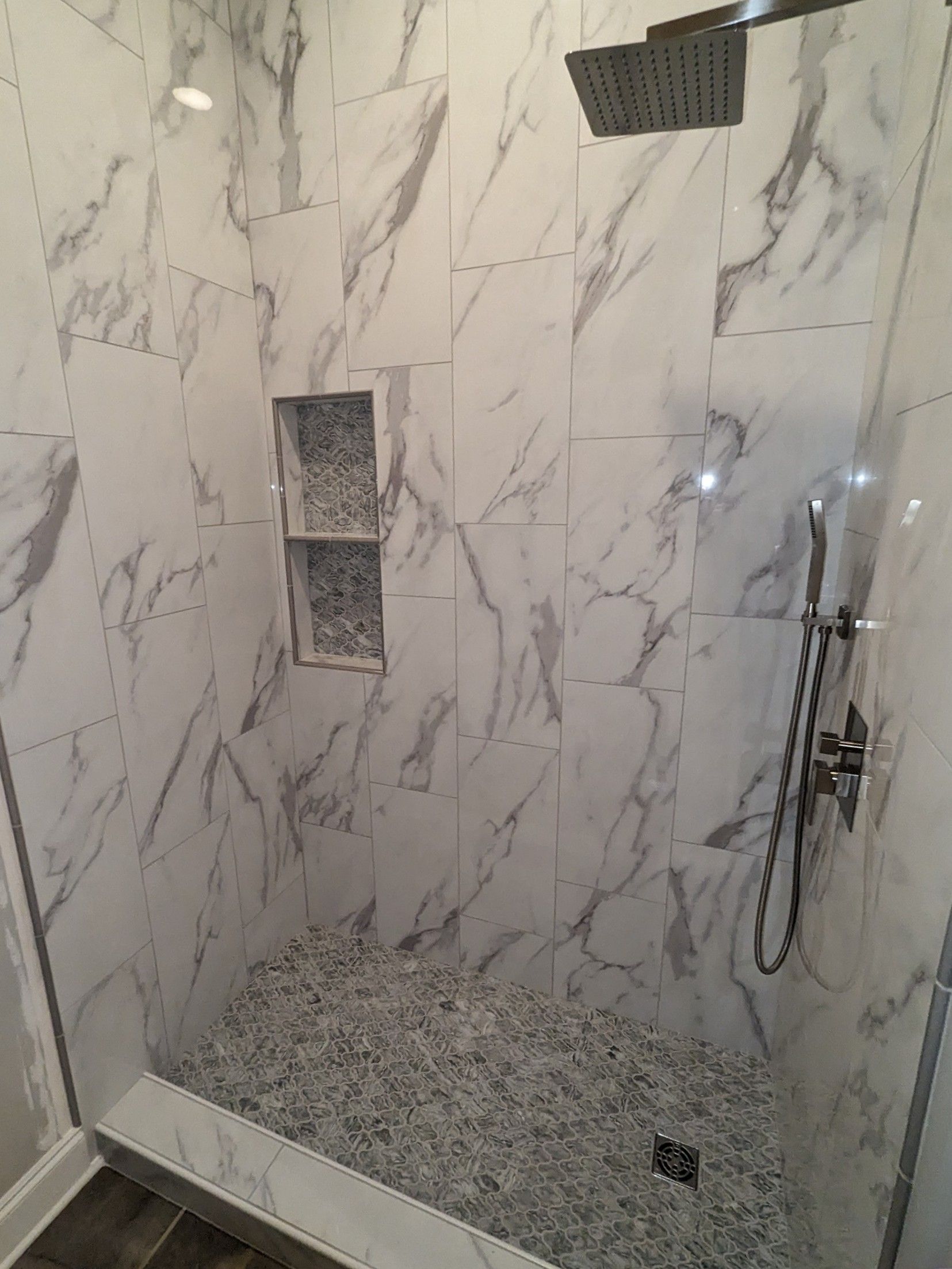 A walk in shower with marble tiles and a shower head with the full tile remodel