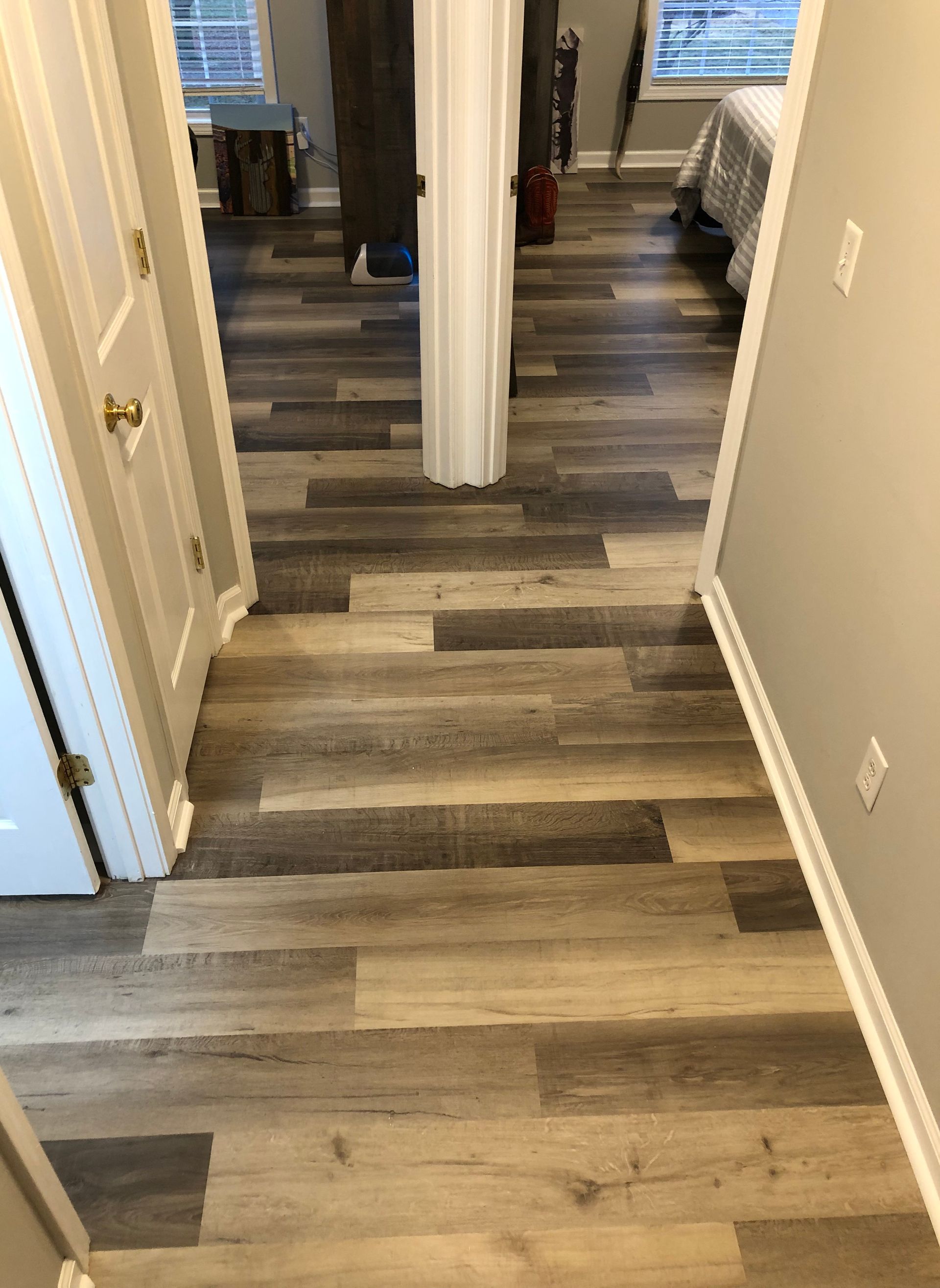 A hallway with a wooden floor leading to a bedroom.