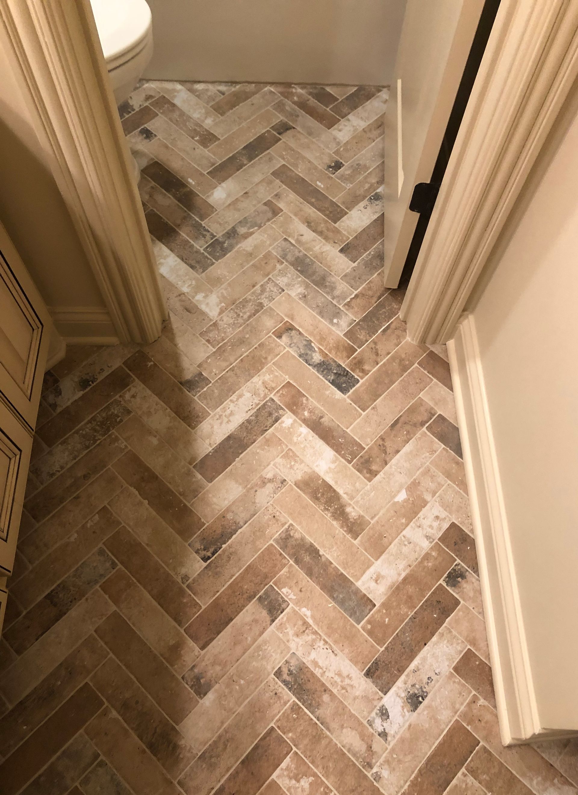 A bathroom with a herringbone tile floor and a toilet.