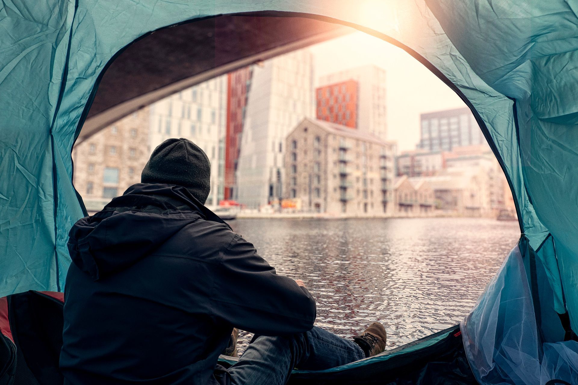 A man is sitting in a tent looking out over a body of water.