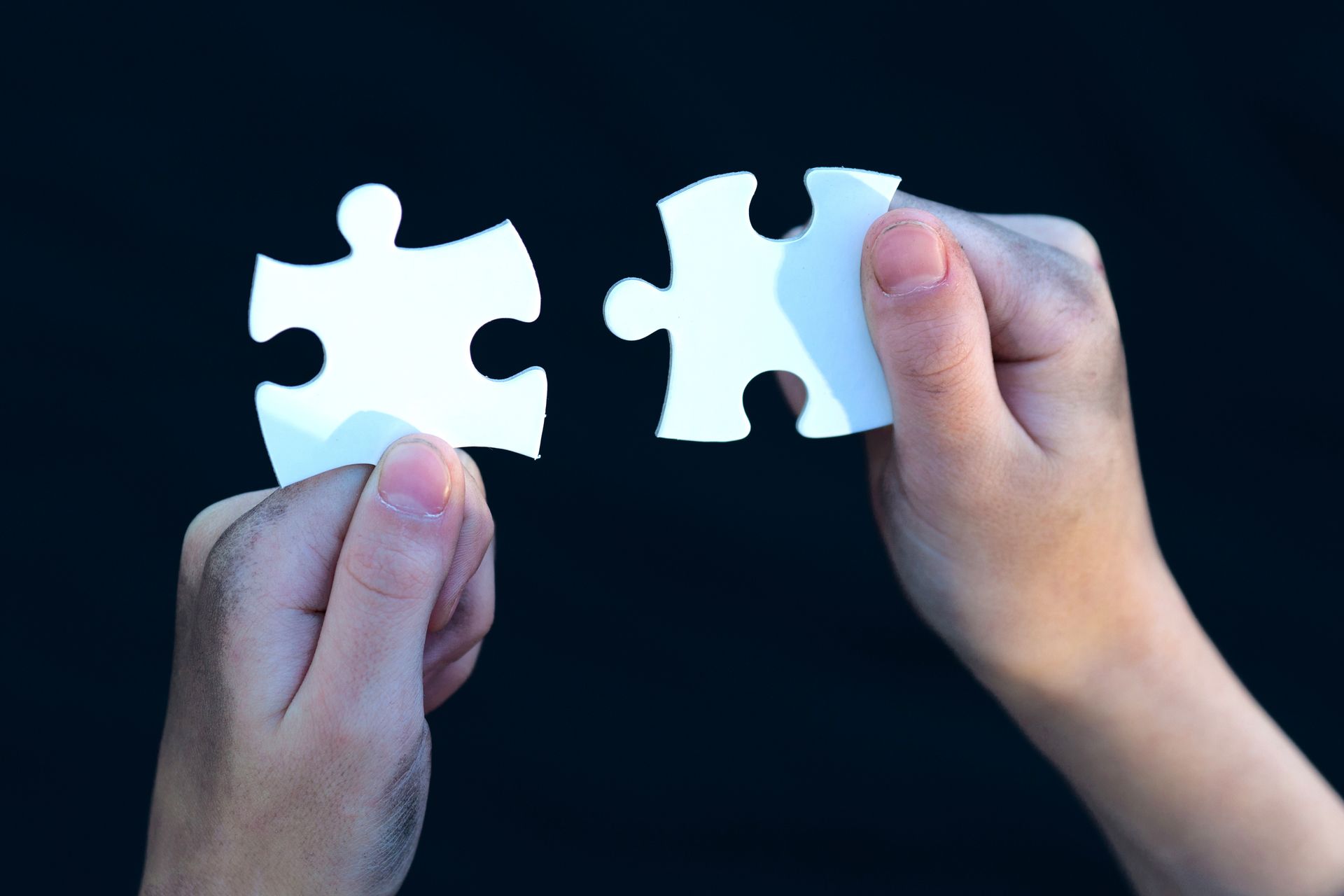 A person is holding two white puzzle pieces in their hands