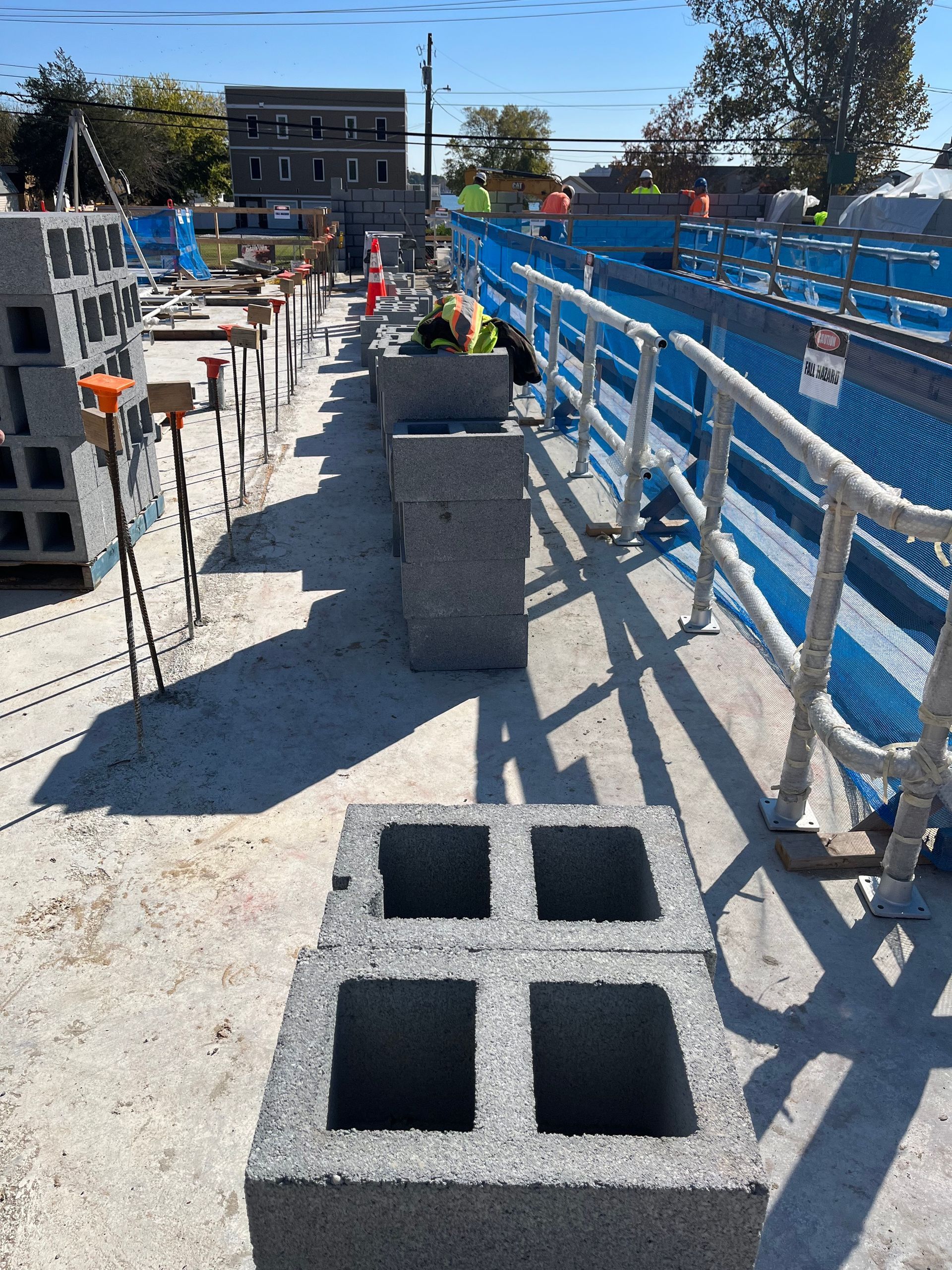 Construction walkway with cinder blocks, concrete barriers, and blue safety fencing along a street under clear sky