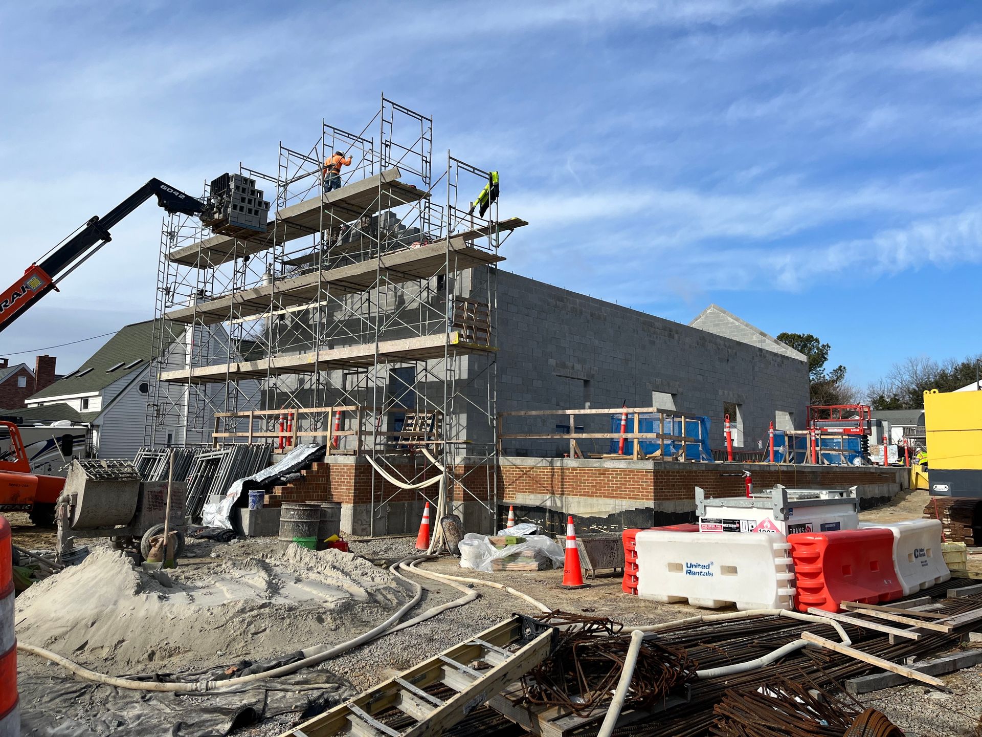 Construction site with scaffolded building, crane arm, cones, and debris under a blue sky