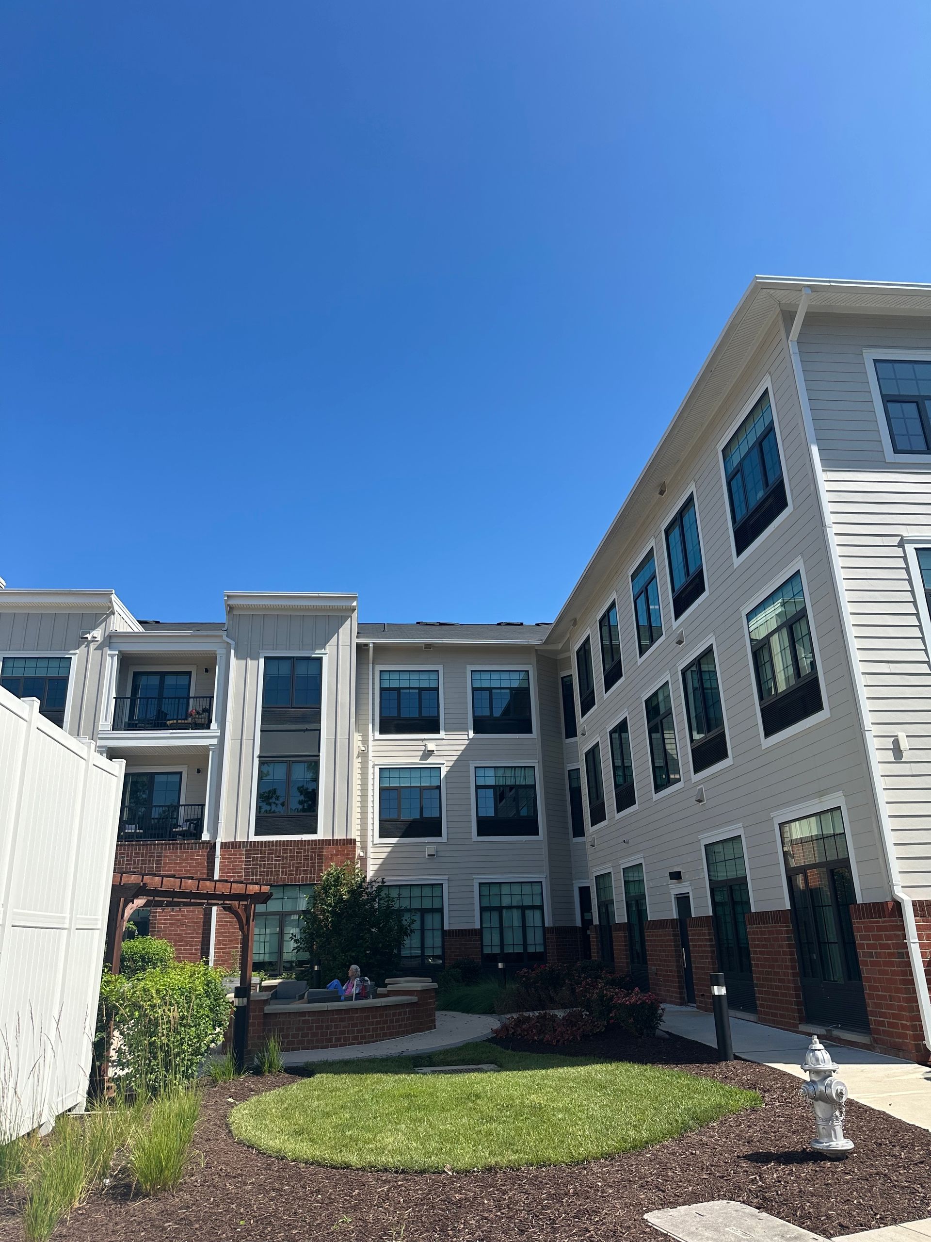 Modern apartment building with white siding, brick accents, and a small courtyard under a blue sky