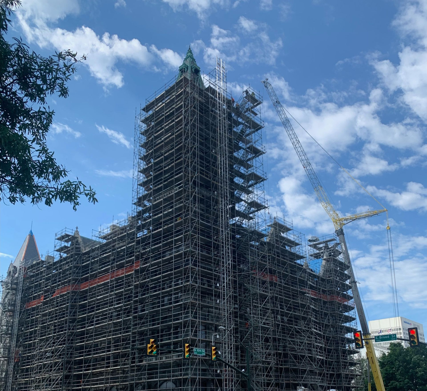 Scaffolded historic building under renovation against a blue sky, with cranes and traffic lights below