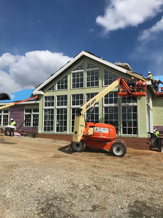 Construction equipment working on a house with tall windows under a blue sky
